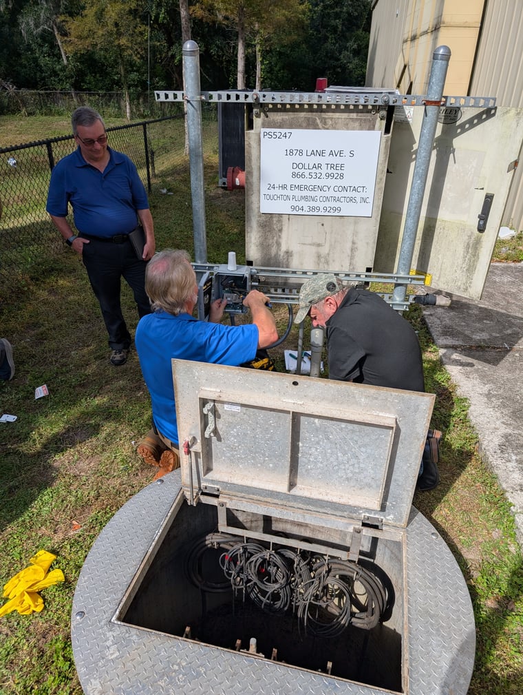 Three technicians working at a lift station panel over an open wet well