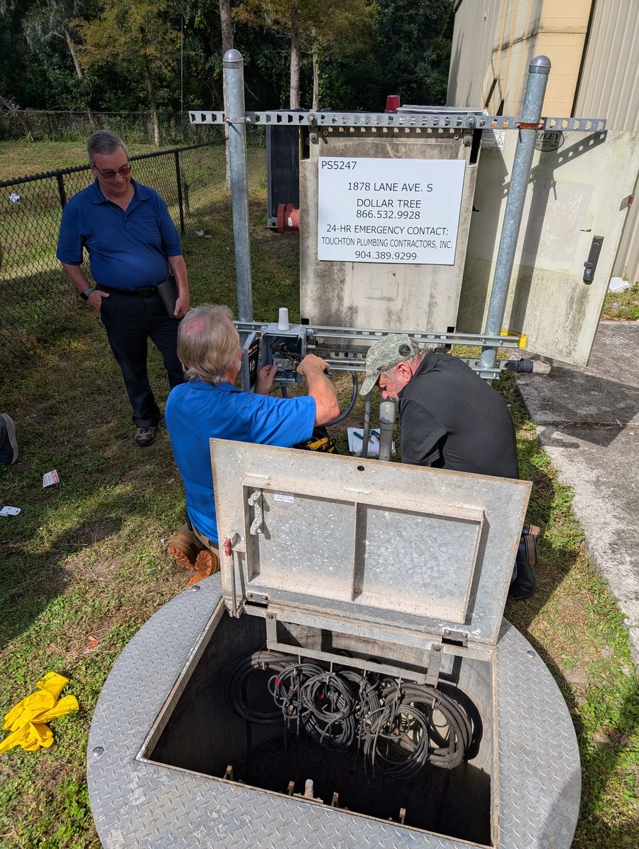 Operators inspecting a site cabinet beside an open wet well